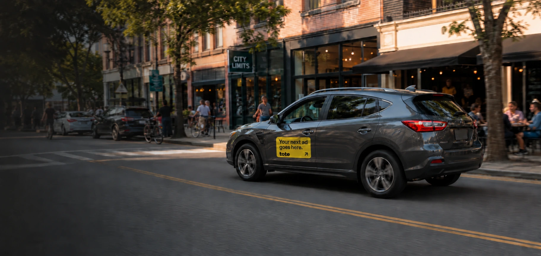 A Tote campaign car moving past shops and cafes on a neighborhood street
